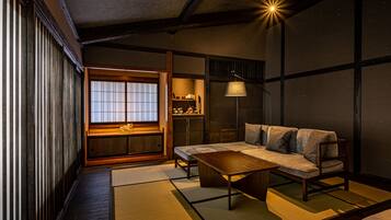 Una habitación japonesa tradicional con suelo de tatami, una mesa baja de madera, un sofá y una ventana con celosías shoji.