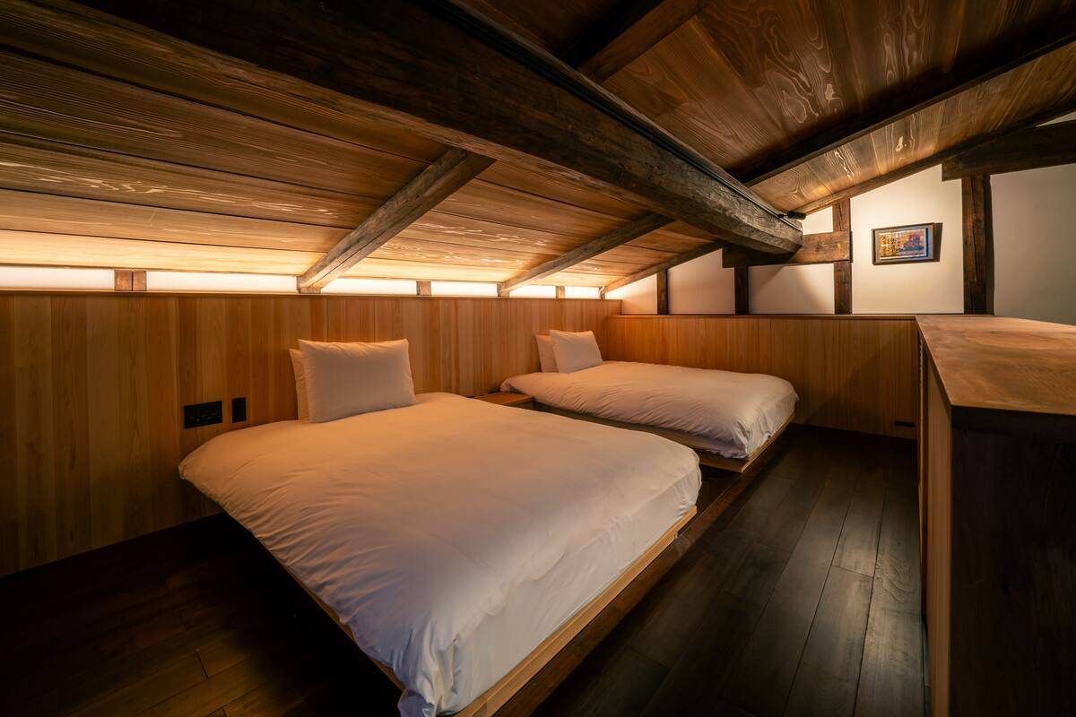 A room with two beds, wooden walls, and a sloped ceiling with exposed beams.