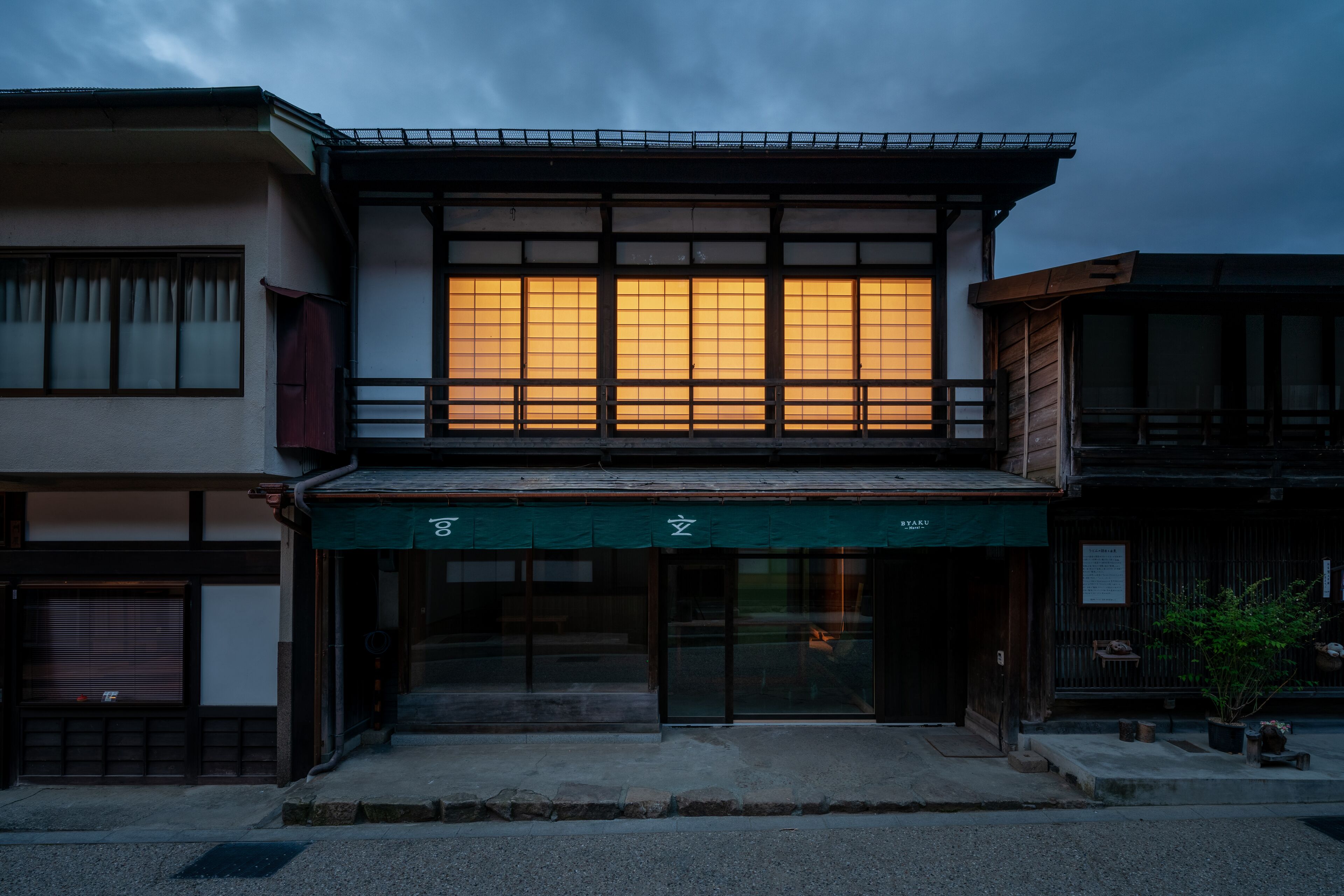 Un edificio japonés tradicional con un amplio ventanal iluminado, un toldo verde y fachada de madera.