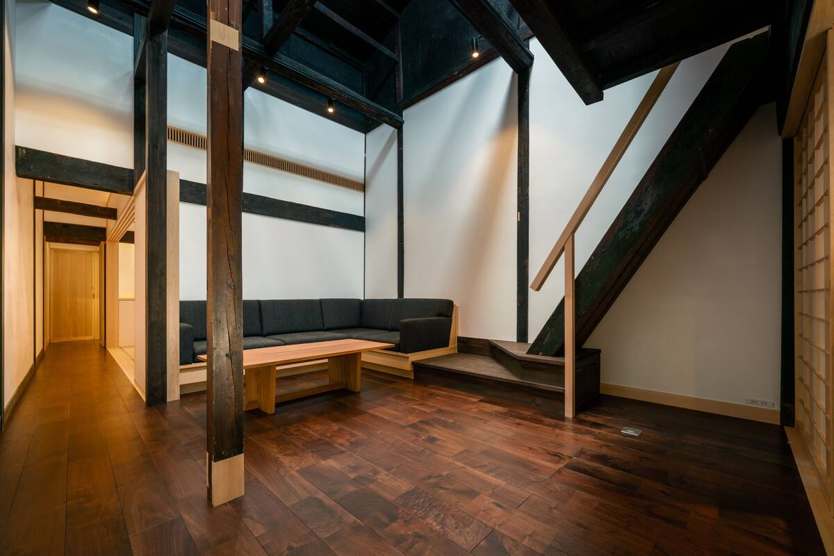 A modern interior with a wooden floor, a built-in bench, a dark-colored sofa, and a staircase.