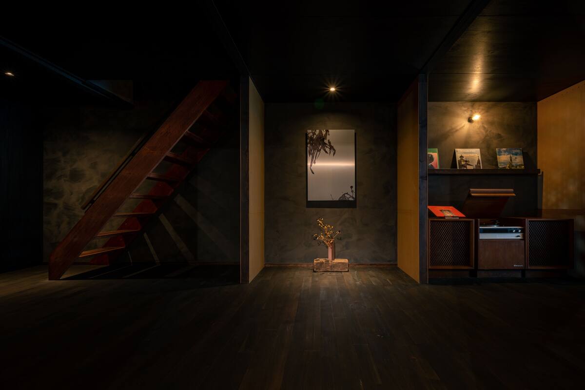 A modern interior with a wooden staircase, a minimalist wall art piece, and a small table with a vase.