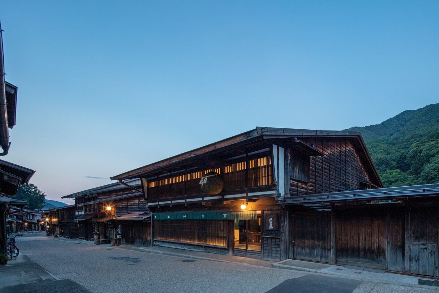 A traditional wooden building with a sloped roof, multiple windows, and a street in front.