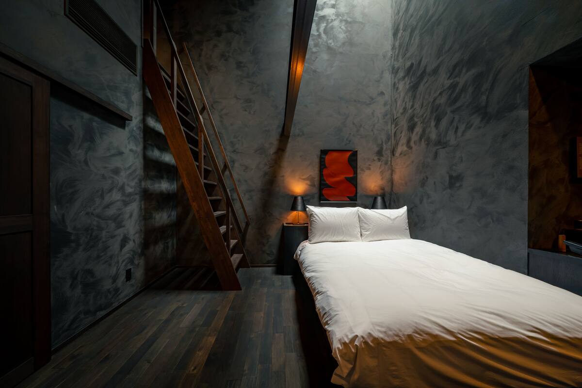 A bedroom with a wooden staircase, a bed with white bedding, and a wall-mounted abstract art piece.