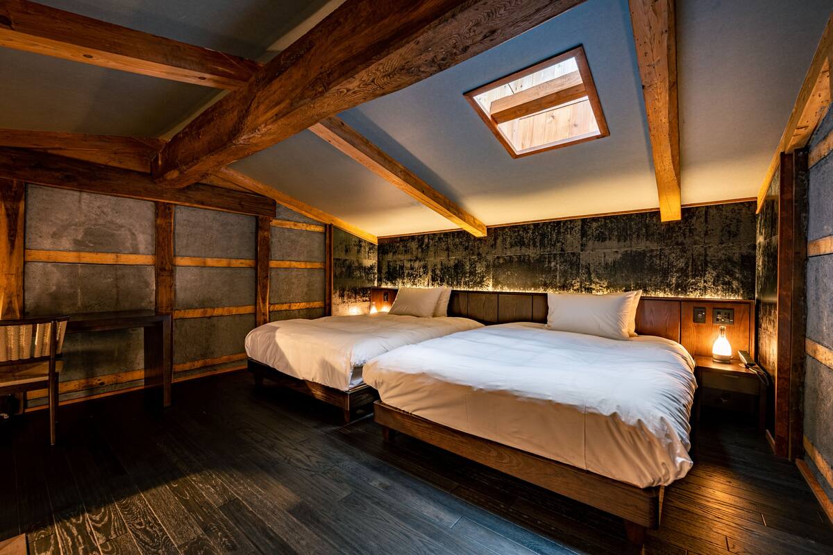 A bedroom with two beds, wooden beams, a skylight, and a stone wall.