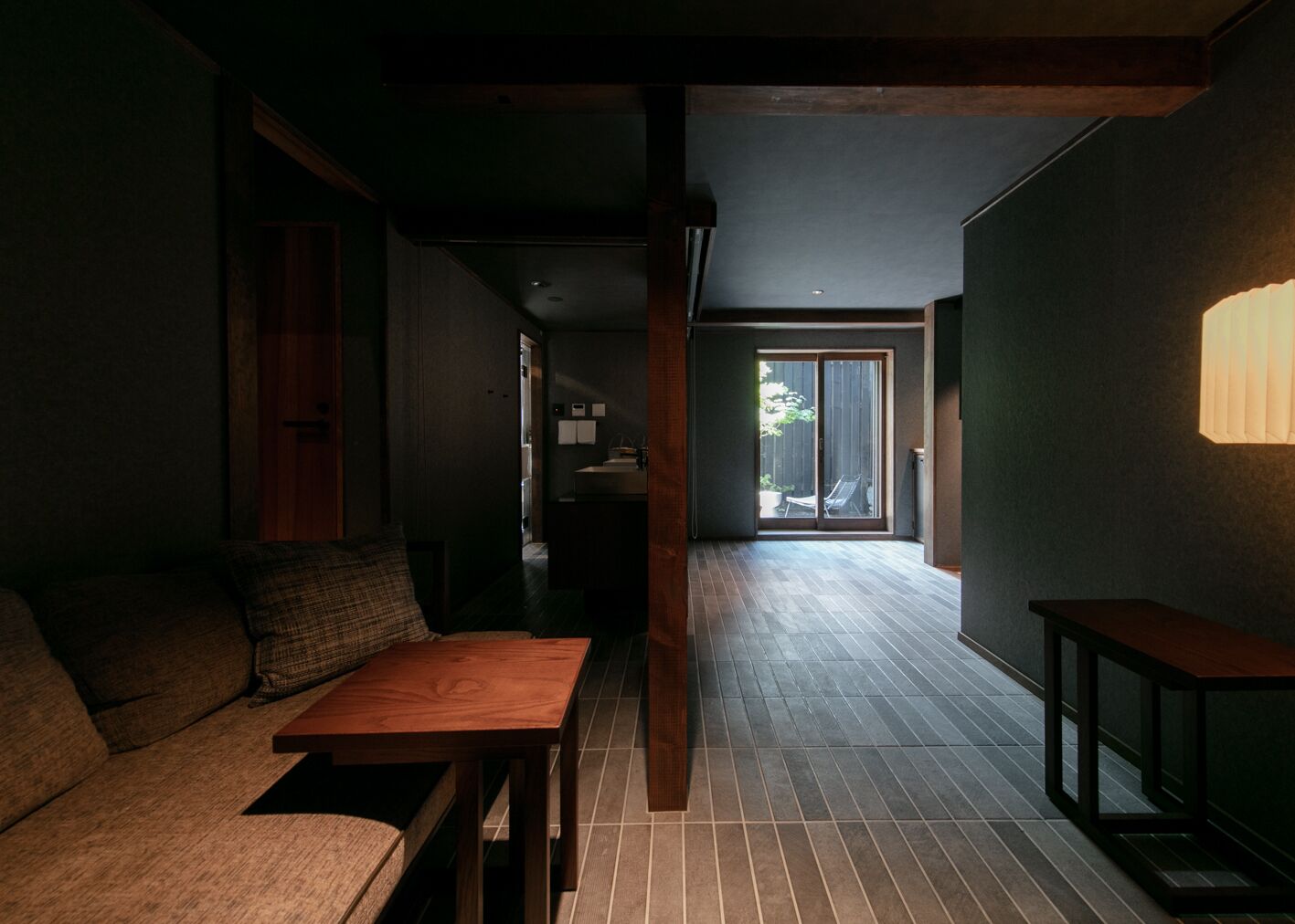 Un intérieur moderne avec un banc en bois, un canapé et une table. Une porte-fenêtre coulissante donne accès à un espace extérieur.