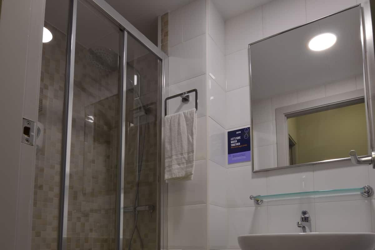 Un baño con ducha de vidrio, un lavamanos con espejo y suelo de baldosas.