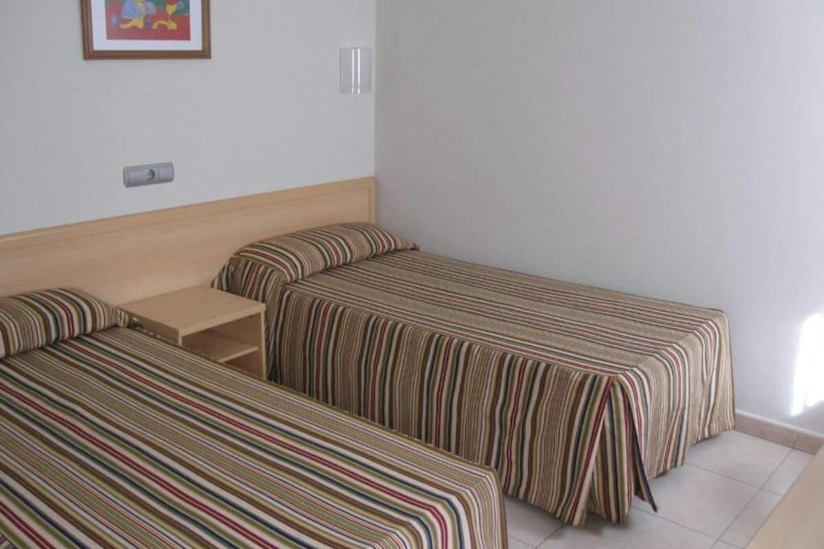 Una habitación con dos camas individuales, una mesita pequeña y un cuadro en la pared.