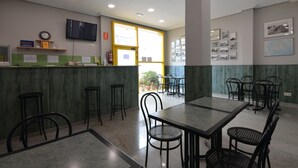 Un restaurante con mostrador, taburetes y mesas. Alrededor de las mesas hay sillas, un reloj en el mostrador y un televisor montado en la pared.