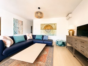 A modern living room with a sectional sofa, a flat-screen TV, a decorative rug, and a wall-mounted light fixture.