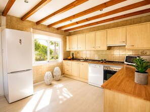 Una cocina moderna con vigas de madera, un refrigerador blanco y un ventanal con vistas a zonas verdes.