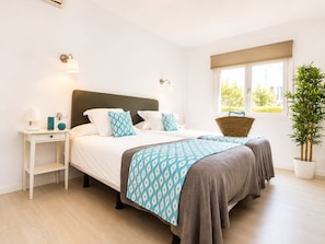 A double bed with a dark headboard, two bedside tables, a bedside lamp, and a window with a view of greenery.
