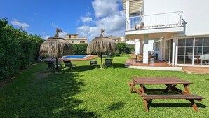 A well-maintained backyard with a swimming pool, two thatched umbrellas, and a wooden picnic table. - Beach Houses Playa de Muro twins SEGALLS Y FOTGES (Muro)