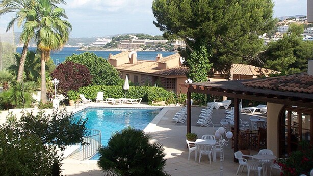 A poolside area with lounge chairs and umbrellas, overlooking a body of water and buildings in the distance. - Casa vida 1 bedroom · Family Friendly Apartment ¨Casa Vida¨ 1 Bedroom (Santa Ponça)
