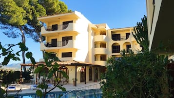 Un hotel de varios pisos con balcones, piscina y abundante vegetación.