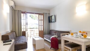 A hotel room with a sofa, a small table, a dining table, a TV mounted on the wall, and a window with curtains. - Casa vida 1 bedroom · Family Friendly Apartment ¨Casa Vida¨ 1 Bedroom (Santa Ponça)