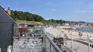 Una località costiera con una passeggiata che si affaccia sulla spiaggia, un ponte e una collina alberata.