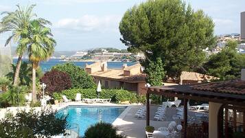 Zona junto a la piscina con sillones y sombrillas, con vista a un cuerpo de agua y edificios a lo lejos.
