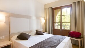 A hotel room with a bed, bedside tables, a nightstand, a window with curtains, and a red suitcase on a small table. - Casa vida 1 bedroom · Casa vida 1 bedroom · Family Friendly Apartment ¨Casa Vida¨ (Santa Ponça)