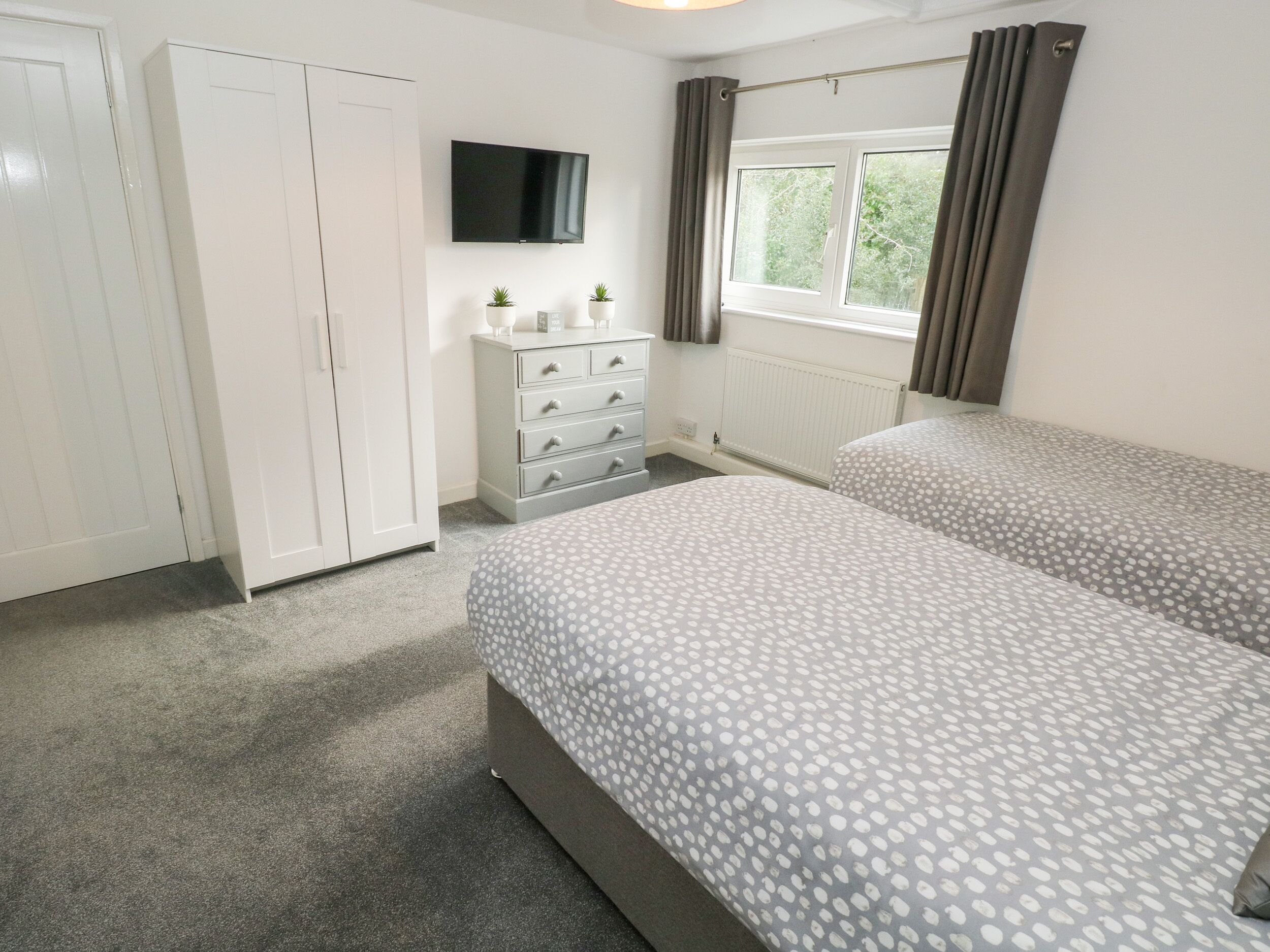A bedroom with two beds, a dresser, a TV, and a window with curtains.