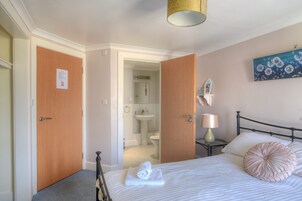 Habitación de hotel con cama, mesita de noche con lámpara, un cuadro en la pared y un baño visible a través de una puerta abierta.