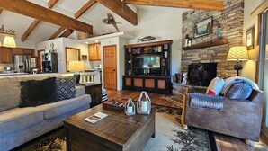 A spacious living room with a fireplace, wooden beams, a stone accent wall, and a cozy seating area. - Cozy Bear Lodge | BBQ | Pet Friendly | Summer Pool (Incline Village)