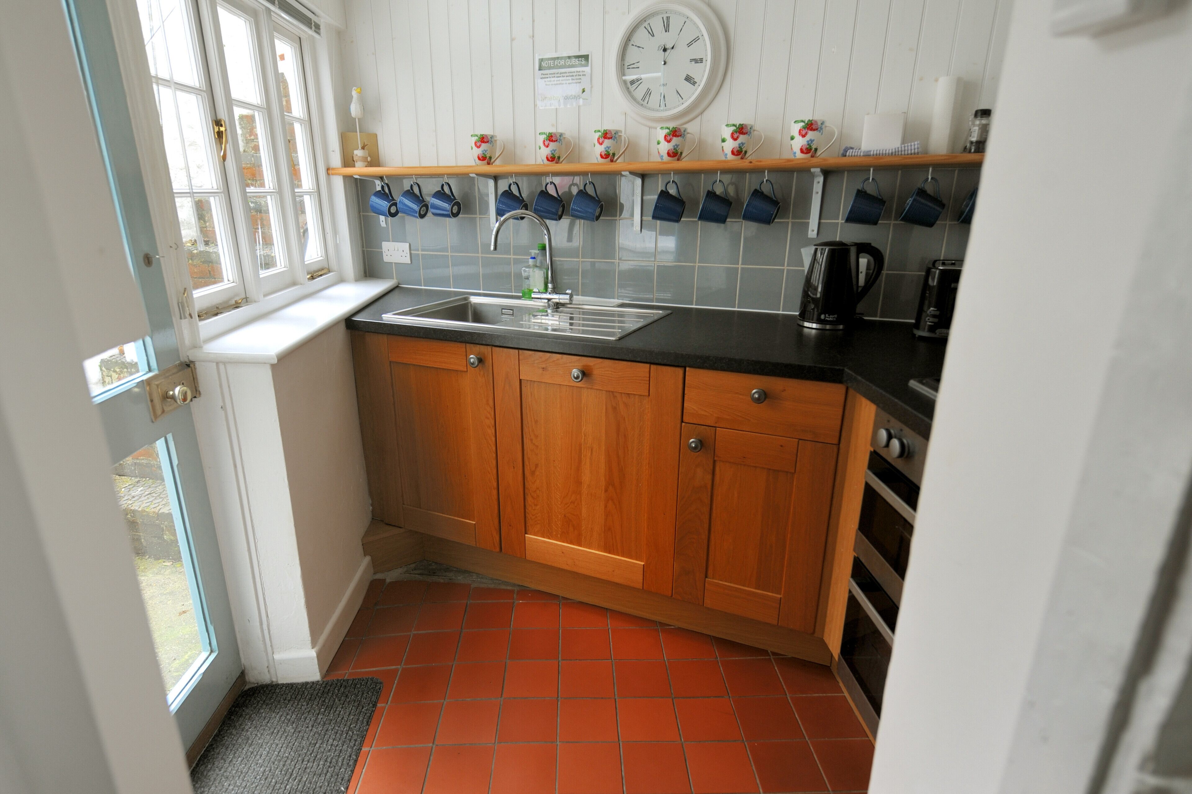 A kitchen with wooden cabinets, a black countertop, a sink, a coffee maker, and a clock on the wall.