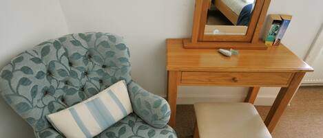 A room with a tufted armchair with leaf patterns, a wooden desk with a mirror, and a small stool.