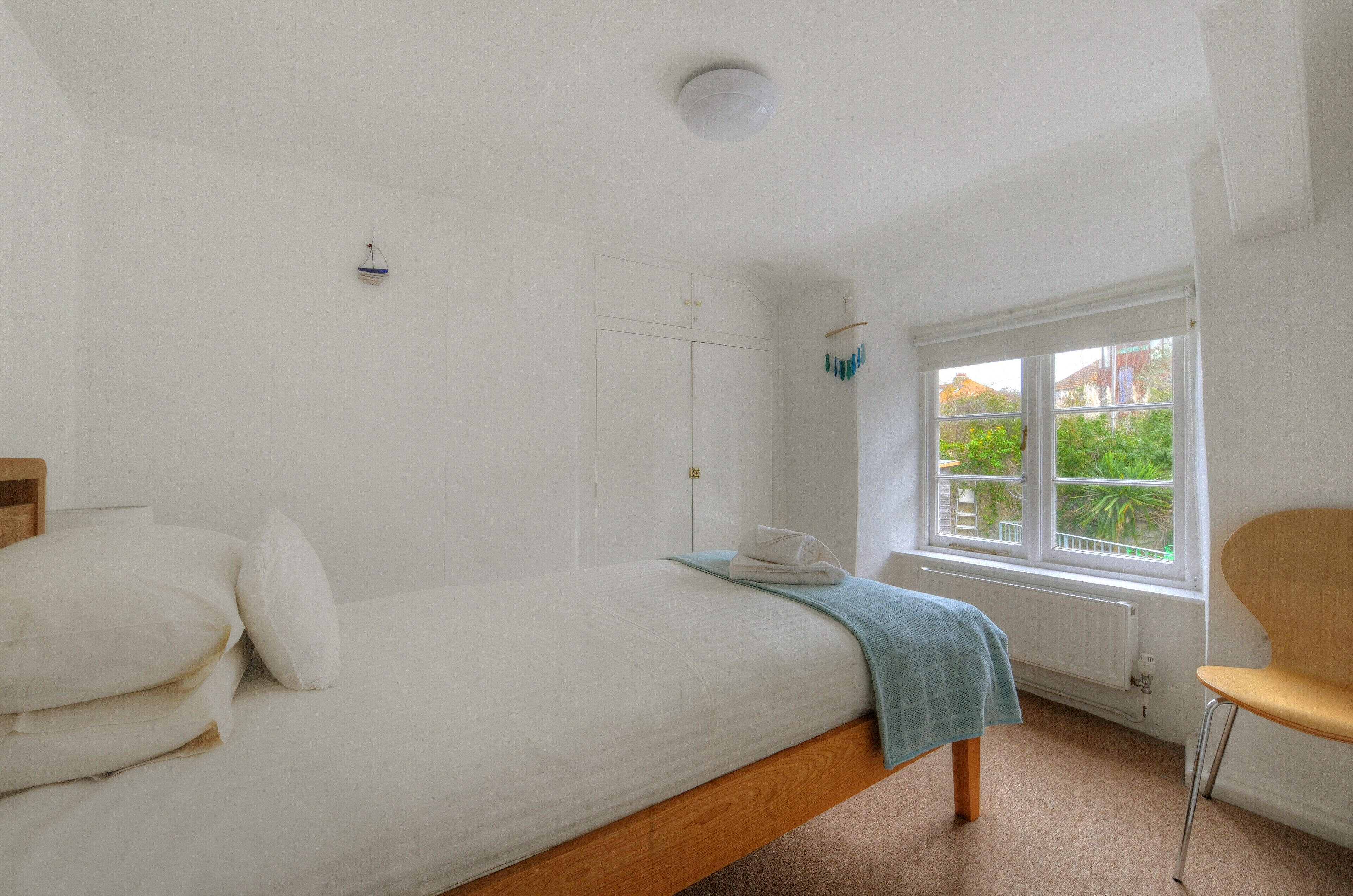 A bedroom with a bed, a window with a view of greenery, a radiator, and a chair.