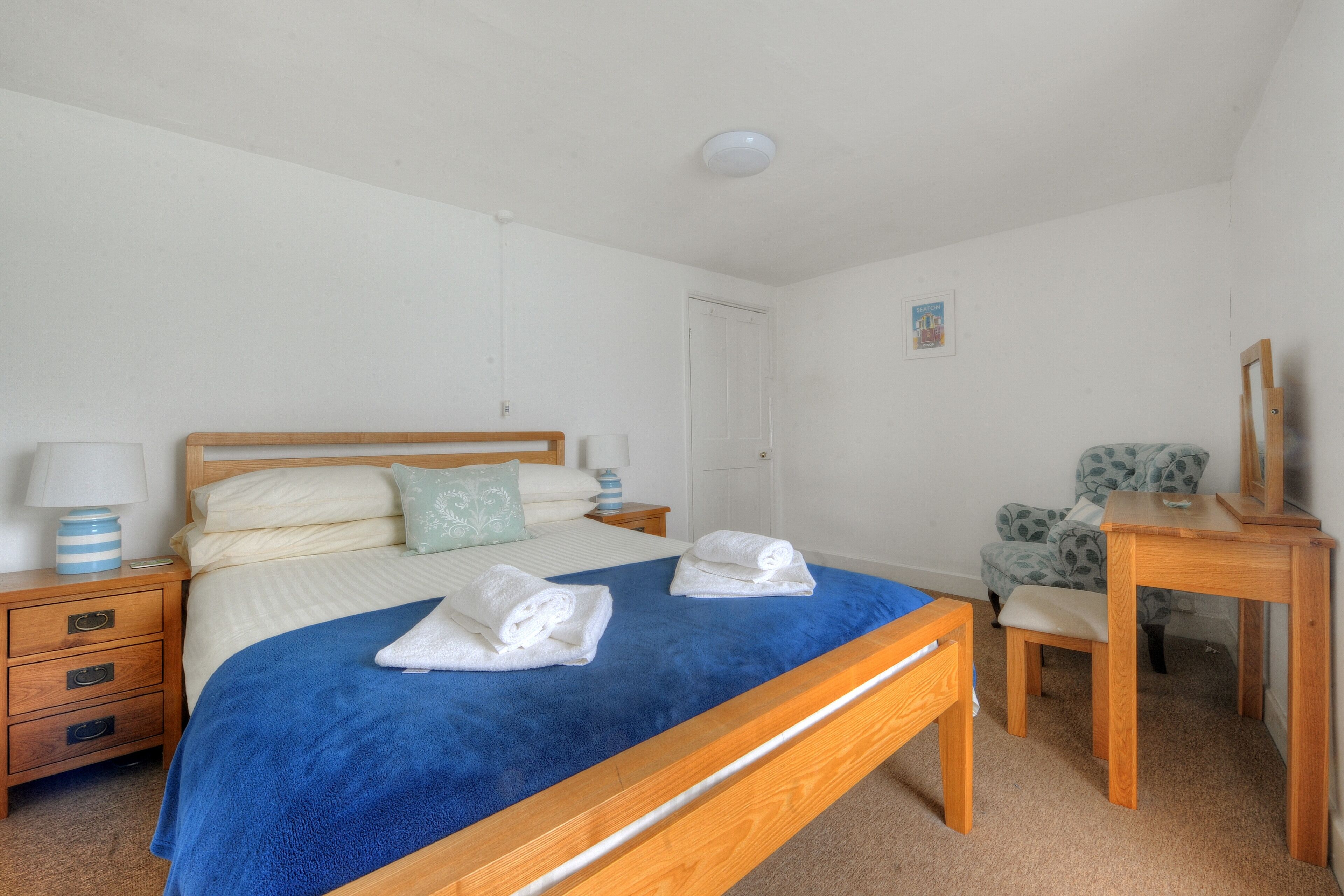 Quarto com cama de madeira, mesa de cabeceira com abajur, cadeira e escrivaninha com espelho.