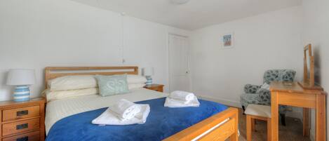 Quarto com cama de madeira, mesa de cabeceira com abajur, cadeira e escrivaninha com espelho.