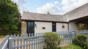 A quaint cottage with a stone facade, a dark door, and a white picket fence. - Ash Cottage (Ilfracombe)