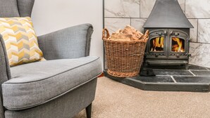 A grey sofa with a chevron-patterned pillow, a wicker basket filled with logs, and a black wood-burning stove. - Ash Cottage (Ilfracombe)
