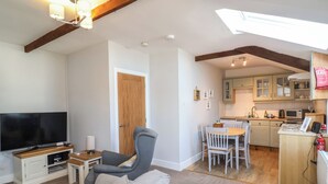 A living room with a sofa, TV, and a dining area with chairs and a table. - Ash Cottage (Ilfracombe)