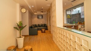 Een hotel lobby met een bank, een televisie, een receptiebalie en een plant.