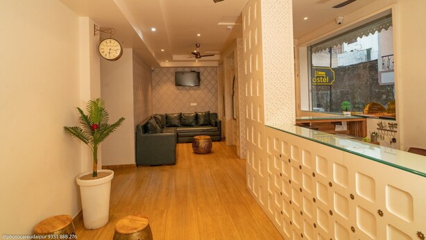 Un vestíbulo de hotel con un sofá, un televisor, una recepción y una planta.