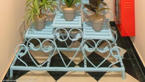Un estrecho pasillo con un arco decorativo azul, un extintor rojo y un soporte metálico azul para plantas con varias macetas.