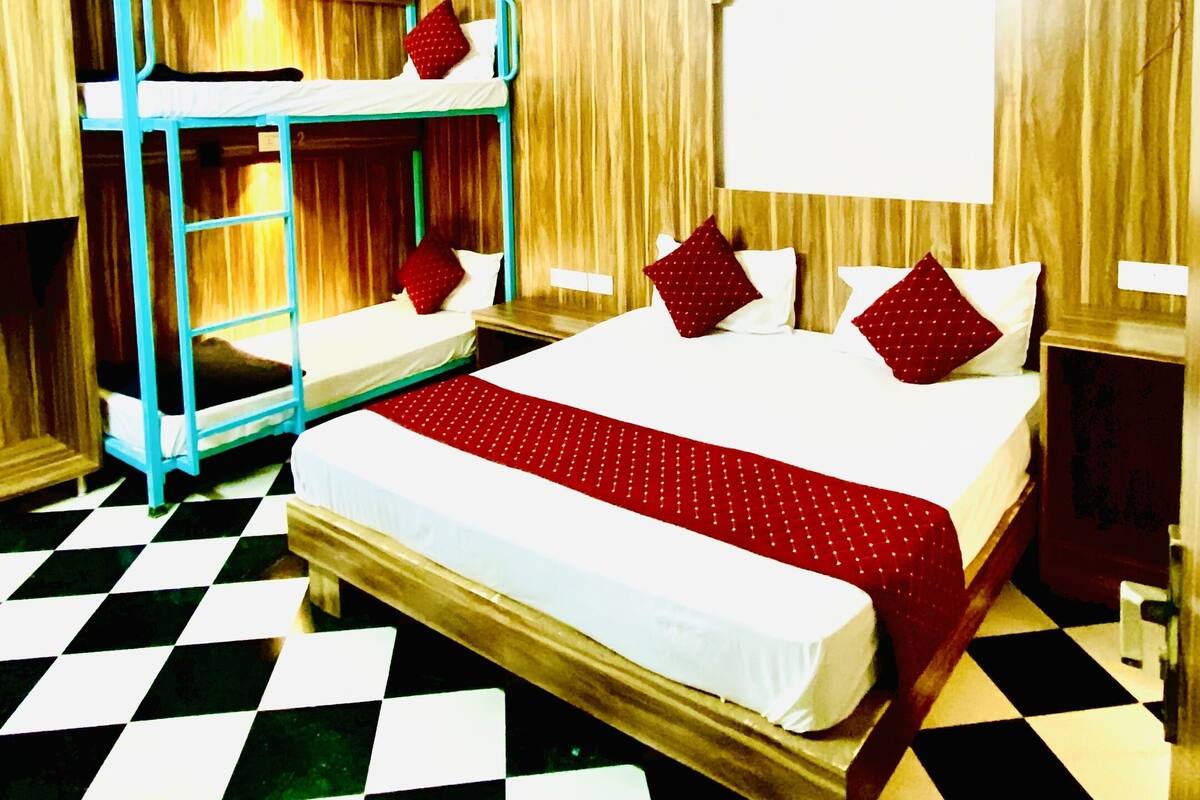 A room with a checkered floor, a bunk bed, a single bed with red bedding, and a wooden ceiling.