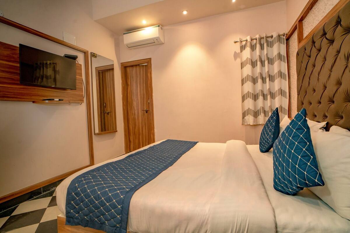 A neatly arranged bedroom with a bed, a television, a wardrobe, and a window with curtains.