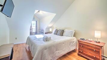 A bedroom with a large bed, wooden floor, a nightstand with a lamp, and a TV mounted on the wall.