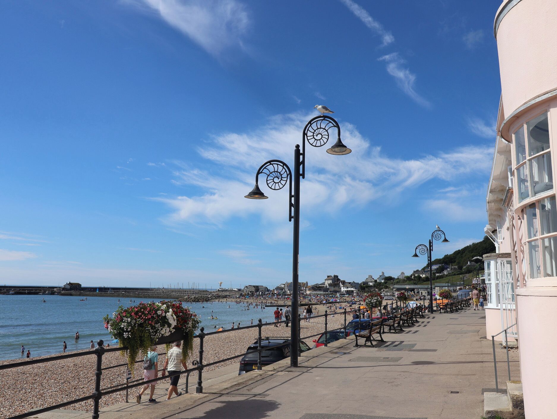 Eine Uferpromenade mit Kiesstrand, einer Reihe von Bänken und einem Gebäude mit großen Fenstern.