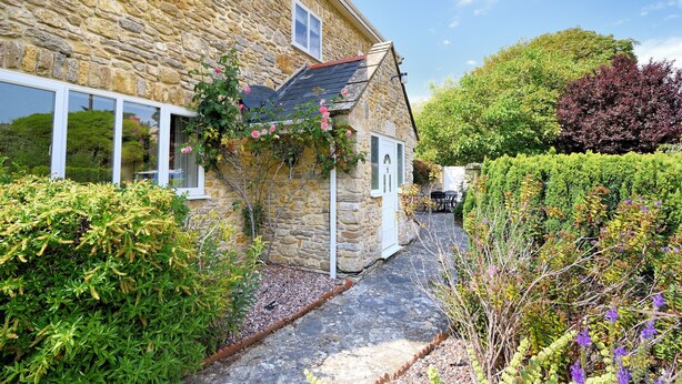A stone building with a sloped roof, a small door, and a window. - Manor Lodge (Bridport)