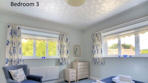 A bedroom with two beds, a chair, a dresser, and a radiator. - Manor Lodge (Bridport)