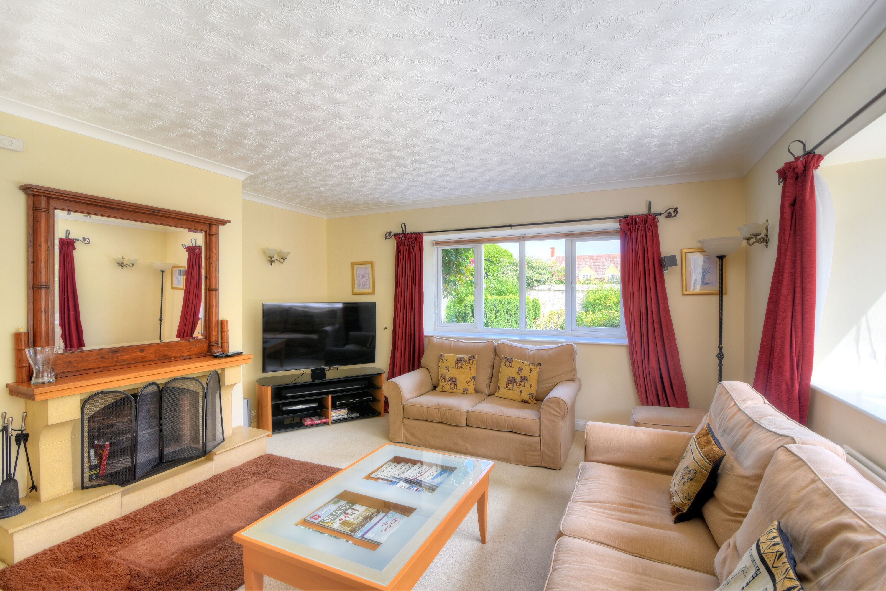 A living room with a fireplace, sofa, television, and a window with curtains.