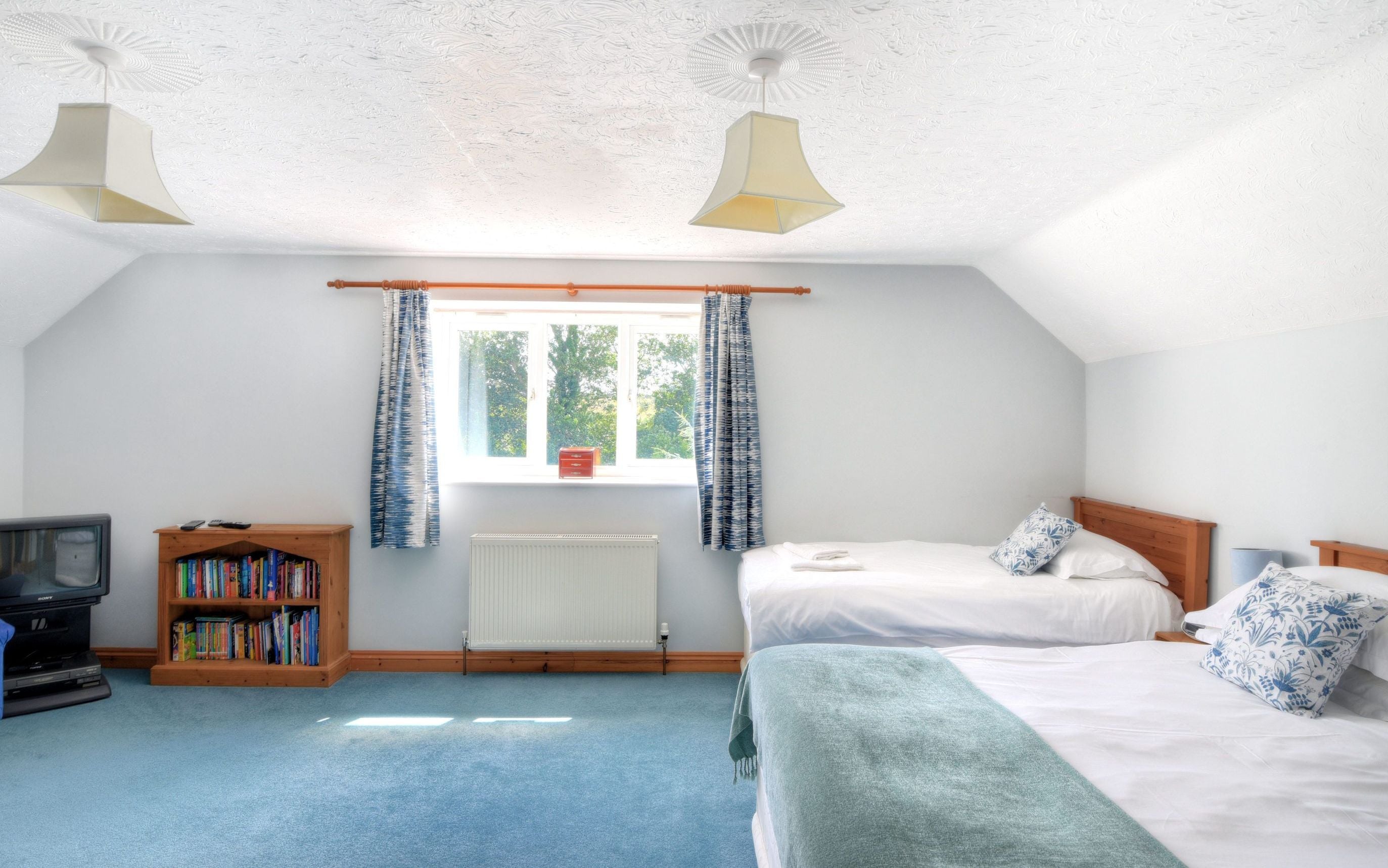 Ein Schlafzimmer mit zwei Betten, einem Bücherregal, einem Heizkörper und einem Fernseher.