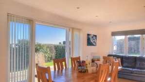 A dining area with a wooden table and chairs, a coffee station, and a view of the garden through large windows. - Pendower (Bridport)