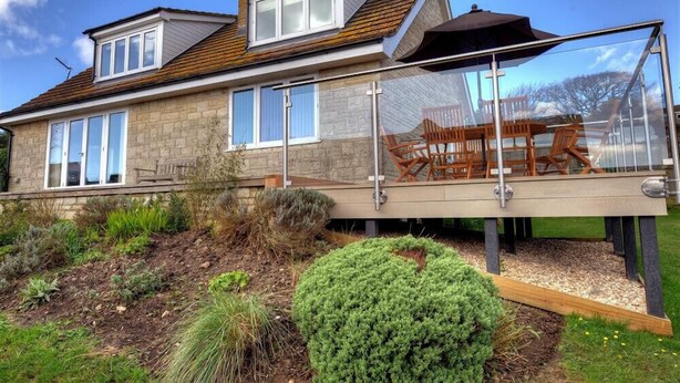 A house with a glass conservatory, stone exterior, and a wooden deck with outdoor furniture. - Pendower (Bridport)