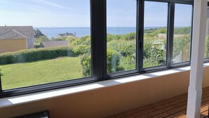 Una stanza con ampie finestre che si affaccia su una zona verdeggiante, un edificio e il mare.