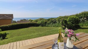 Un patio in legno con una bottiglia di vino e bicchieri, un vaso di fiori e vista sul mare.