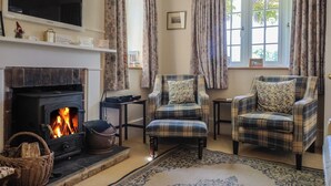 A cozy living room with a fireplace, two plaid armchairs, a television, and a large window with curtains. - Lynch Cottage (Lyme Regis)