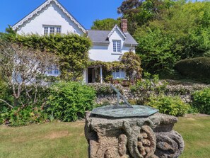 A stone sculpture in a garden with a white house in the background.